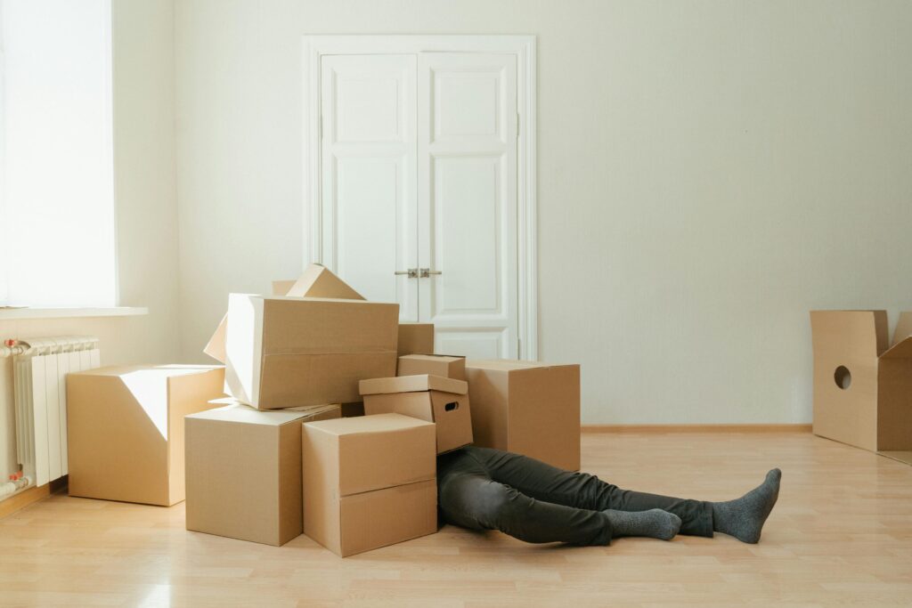 Person on floor surrounded by cardboard boxes during moving; concept of stress and relocation.