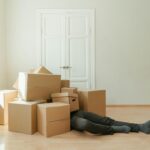 Person on floor surrounded by cardboard boxes during moving; concept of stress and relocation.